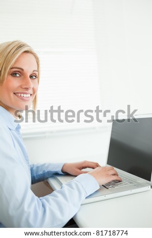 Close up of a gorgeous blonde businesswoman working on laptop looking into camera in her office
