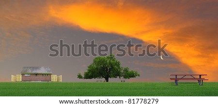 An outdoor restroom facility and a large oak tree with picnic tables at a park on a summer day with a gorgeous sunset red sky and moon with room for your text.