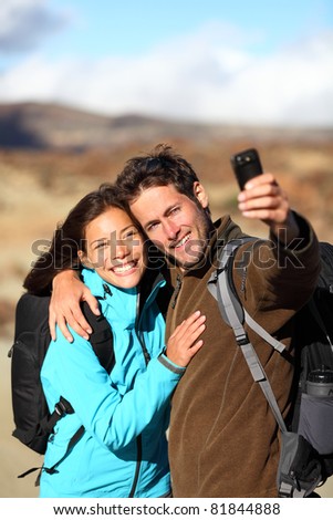 Happy young couple smiling hiking outdoors on travel taking self portrait picture with camera or mobile phone. Asian Caucasian couple on holidays. Photo from volcano Teide, Tenerife, Canary Islands