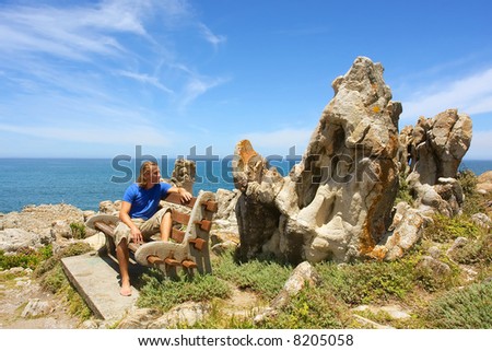 Man sits on bench next to amazingly shaped rocks. Shot on Cliff Path near Hermanus, Walker Bay, Western Cape, South Africa.