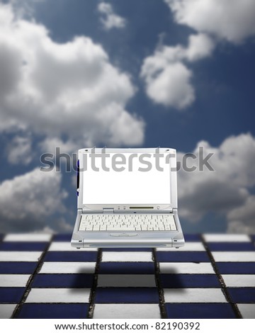 A mobile computer laptop with a blank screen for copyspace text, floating over a a blue and white chess board grid with a surreal blue cloudy sky background.