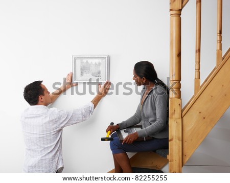 mid adult multiethnic couple hanging pictures to the wall and smiling. Horizontal shape, copy space