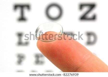 Contact lens on finger and snellen eye chart. The eye test chart is shown blurred in the background. Royalty-Free Stock Photo #82276939