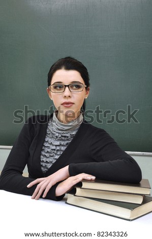 Young beautiful teacher leaning on the books on the blackboard background