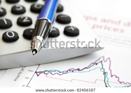 Calculator and ballpoint pen on top of financial figures and graphs