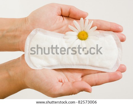 Panty liner and daisy flower on the female palms on a white background.
