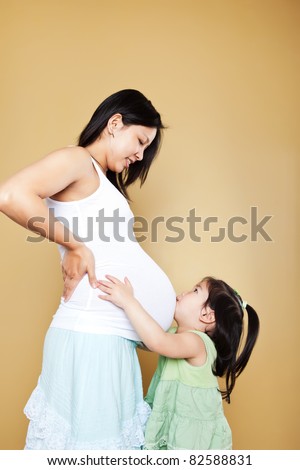A shot of a little Asian girl kissing her pregnant mother on the stomach