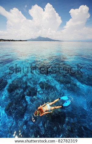 Young woman in swimsuit snorkeling in clear shallow tropical sea over coral reefs