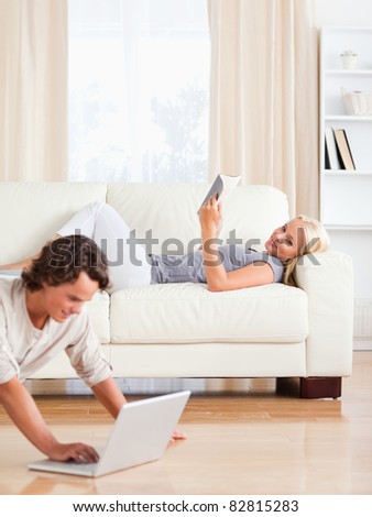 Portrait of a man using a laptop while his wife is reading a book in their living room