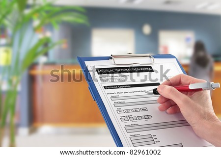 A Hand filling in medical information form with blurred hospital reception area in background