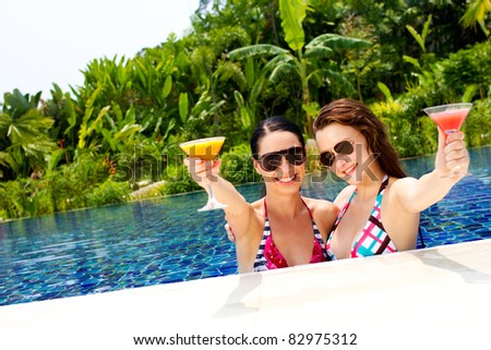 Two beautiful women enjoying their summer vacation with cocktails by the pool