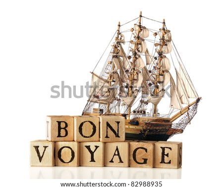 A big sailing ship behind rustic alphabet blocks arranged to say "Bon Voyage.)  Isolated on white.