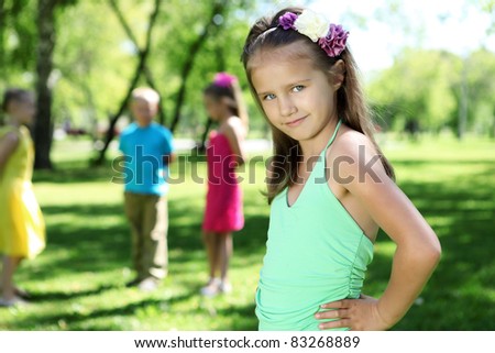 Little girl in bright wear in summer park with friends on the background