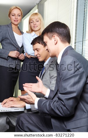 Two businessmen interacting while working with laptop on background of pretty females looking at them