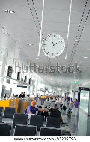 White clock in a waiting lounge in an airport terminal with people sitting in the background