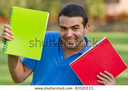 Happy male student with a notebook outdoors and smiling