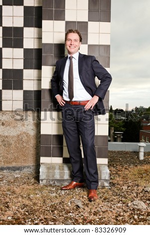 Young business man outdoors on top of building with cloudy sky.