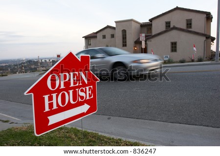 Red and white open house sign with a car passing by and the house in the background