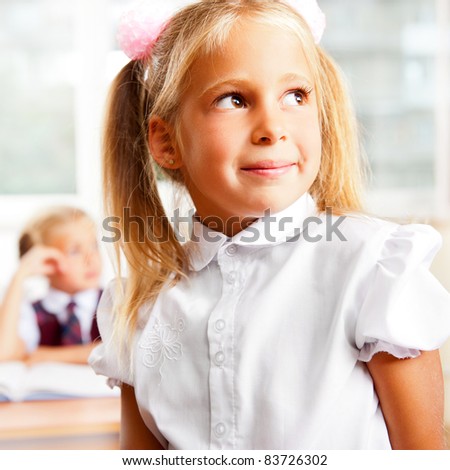 Portrait of a schoolgirl being in a classroom at school with her classmates on the background of photo. She is looking away and daydreaming. Horizontal Shot.