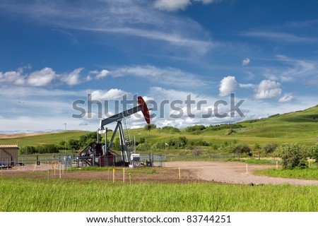 Beautiful landscape with green grass, blue sky and pumpjack. Photo is taken on sunny day of summer in Alberta, Canada.