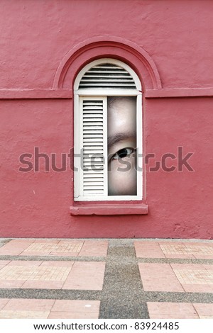 A giant man's eye peeping through a vintage timber louver window on a grungy red mason wall.
