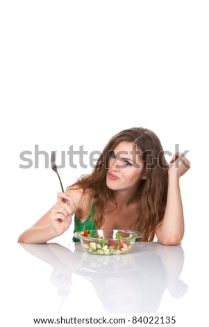 Portrait of attractive young smile woman eating vegetable salad, holding bowl and fork in hand, sitting at the table, isolated over white background