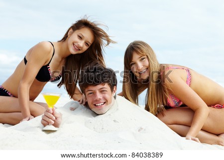 Two girls in bikini and happy guy with cocktail having fun on sandy beach