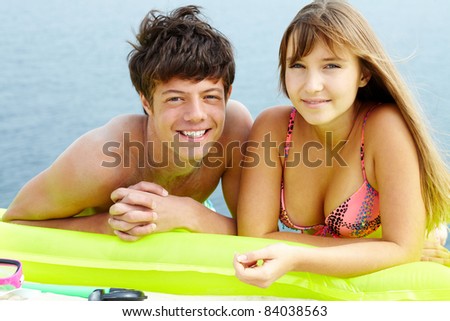 Portrait of teenage girl in bikini and her boyfriend lying on mattress and sunbathing
