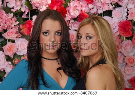 Two beautiful woman standing in front of a wall of roses