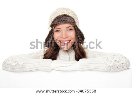 Winter woman sign banner. Cute smiling woman in warm winter sweater and wool cap showing blank white paper poster isolated on white background.
