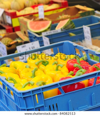 Yellow and red sweet peppers in blue plastic crate on market place, selective focus