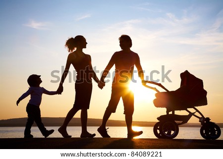 Silhouettes of happy parents walking with child and baby's stroller on the seacoast