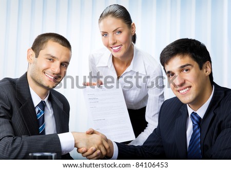 Three happy smiling successful business people handshaking with document at office