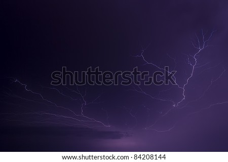 Lightning arcs across the sky illuminating clouds with a purplish flash. Great detail in the branching and forking of the lightning bolts. Photographed in central Indiana in the Midwest of the USA.