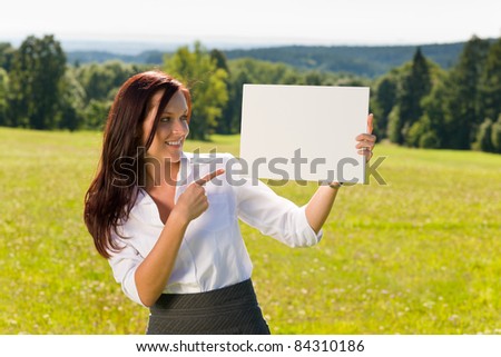 Young businesswoman sunny meadow pointing aside at blank advertising banner