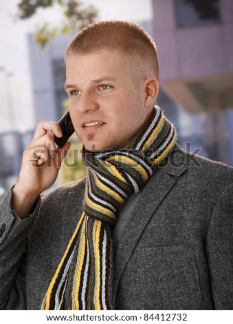 Spring portrait of guy using cellphone, wearing scarf, outdoor picture.?