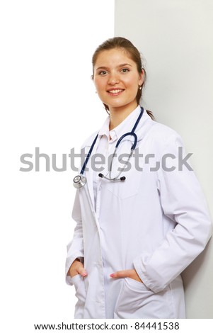 Smiling female doctor with her hands in pockets against the wall