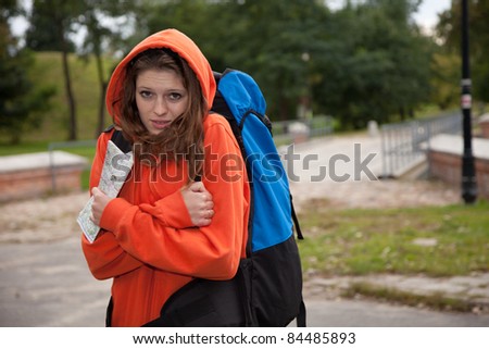 a beautiful caucasian young woman with map in her hands, rucksack on her back standing in a park outdoors in windy day on vacation
