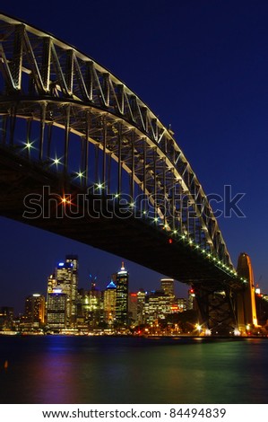 Luminous Sydney Harbor Bridge at night with colorful lighting and the skyline of the city center in vertical frame