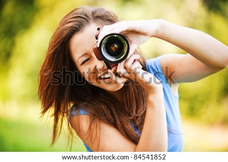 Portrait of beautiful laughing brunette girl wearing blue t-shirt, making photos at summer green park.