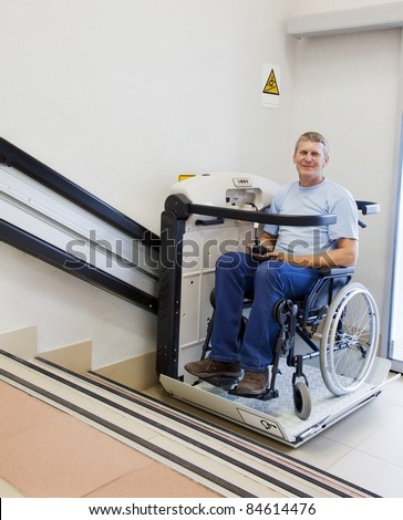 man in an invalid chair walks upstairs on the special elevating device Royalty-Free Stock Photo #84614476