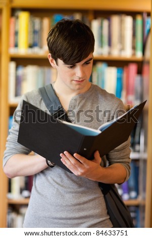 Portrait of a smiling student looking at a binder in the library