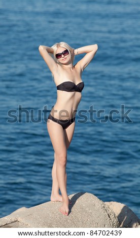 Slim girl in black swimwear and sunglasses at the sea. Young woman looking at camera through sunglasses
