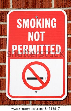Sign hangs on a brick wall warning that smoking is not permitted in the area.