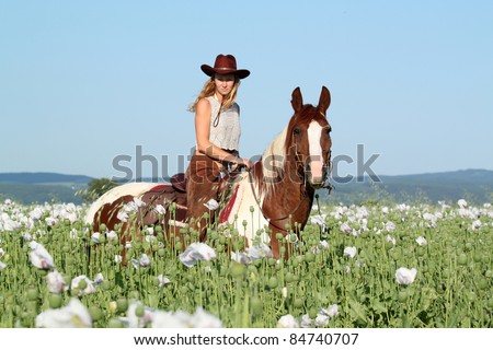 Pretty woman posing on horse in the poppy field