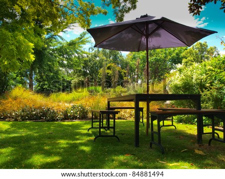 dining table with chairs and parasol in the shade in a lush garden Royalty-Free Stock Photo #84881494