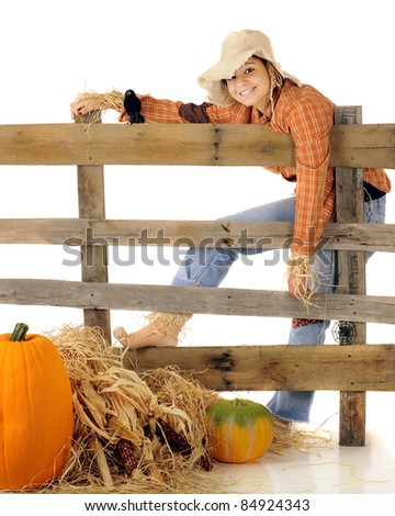 A pretty teen scarecrow flopping over an old rail fence with a hay, pumpkins and Indian corn in the foreground.  On a white background.