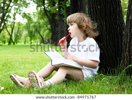 Portrait of little girl reading a book in the summer park