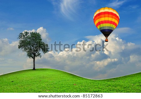 hot air balloon with lonely tree over the green grass field and blue sky