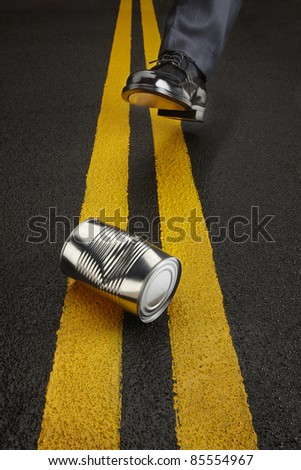 Politician kicks a shiny, dented can down the road toward the camera Royalty-Free Stock Photo #85554967